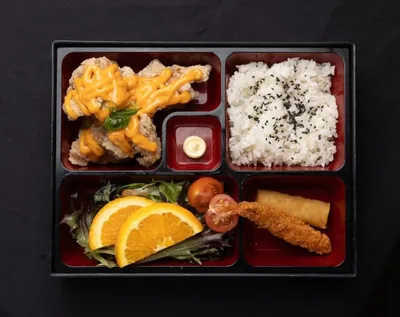 Chicken karaage bento box with rice, salad and sauce.