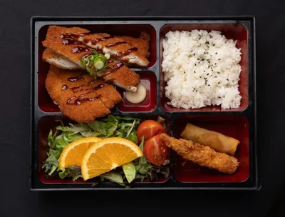 Chicken katsu bento box with rice and spring rolls.