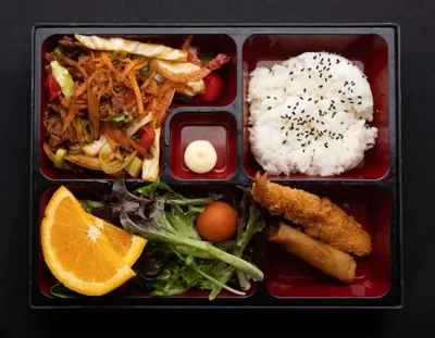 Spicy pork bento box with rice and sides.